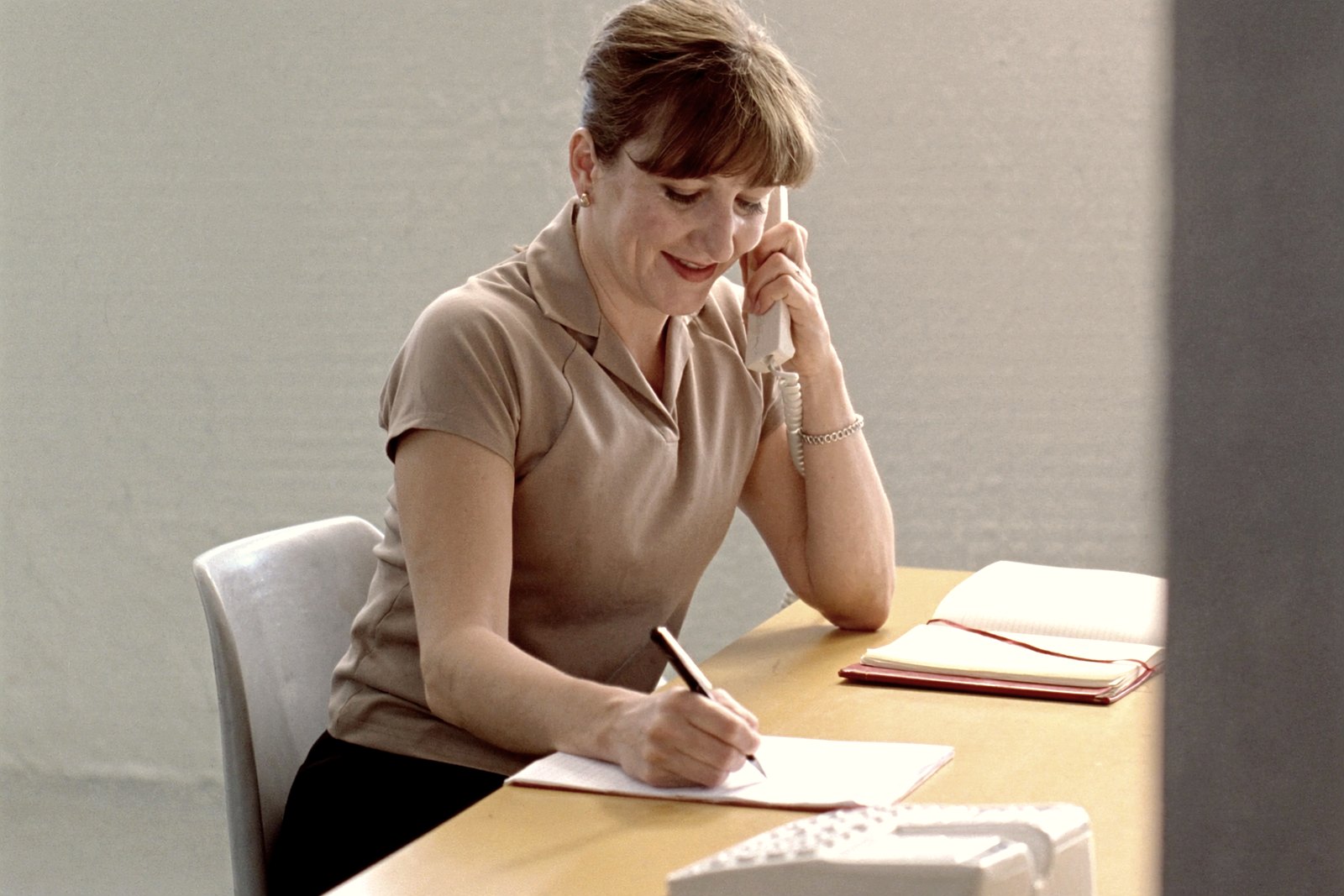 A woman taking a call at her desk and writing a note