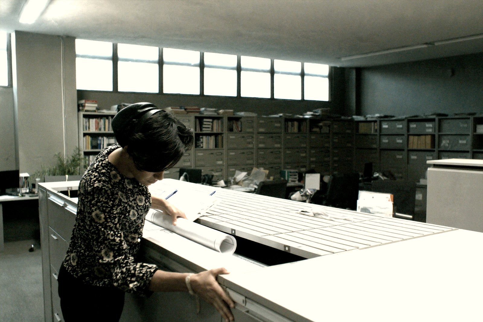 A document controller filing a rolled drawing into a labelled plan chest