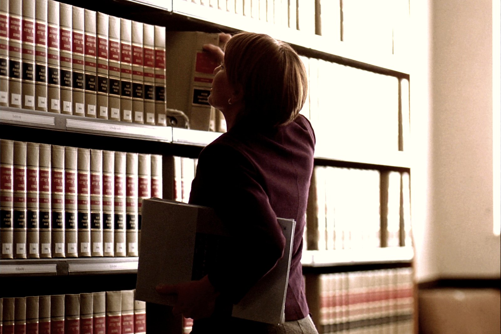 A woman sliding a bound matter file back into place on a shelf